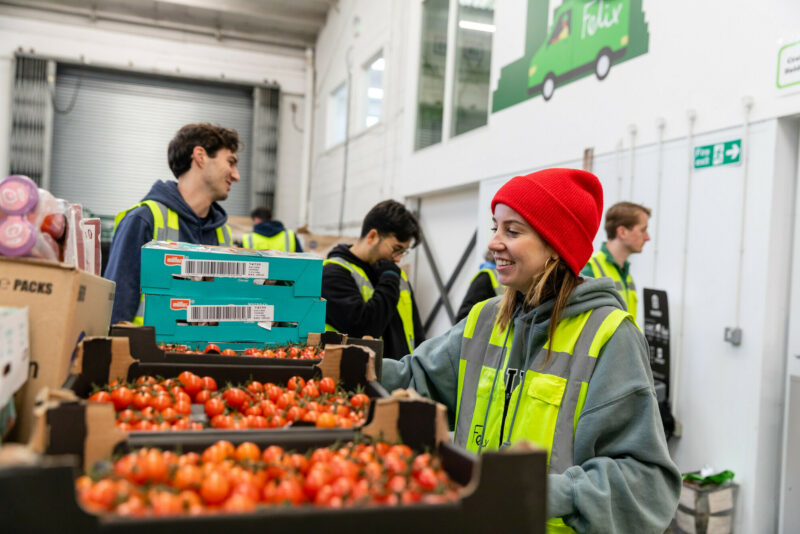 Woman in hi-vis smiling in front of crates of tomatoes